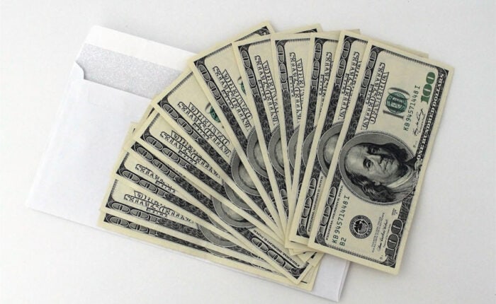 Mehrere 100-Dollar-Scheine fächerförmig auf einem weißen Umschlag ausgelegt.
