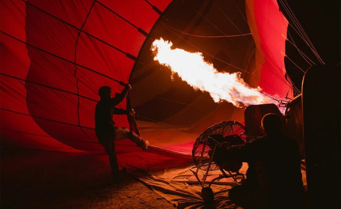 Ein Heißluftballon wird nachts mit einer großen Flamme aufgeheizt, während Menschen daran arbeiten.