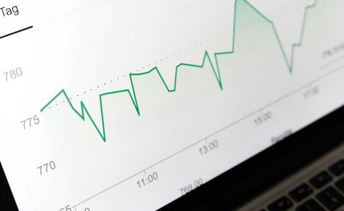 Laptopbildschirm zeigt Kursschwankungen eines Börsencharts mit grüner Linie im Tagesverlauf.