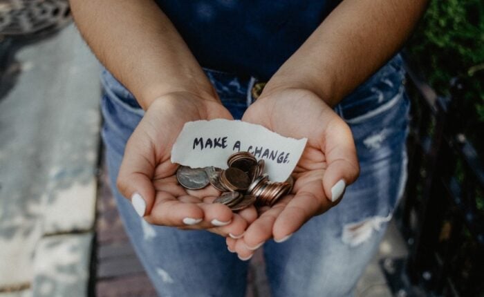 Person hält Kleingeld und ein Papier mit Aufschrift "Make a change" in der Hand.