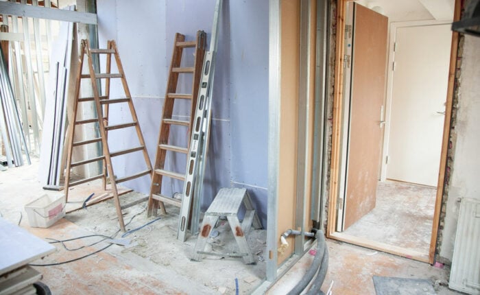 Baustelle eines Innenraums mit Leitern, Metallprofilen und offenen Türen, umgeben von Baumaterialien und Werkzeugen.