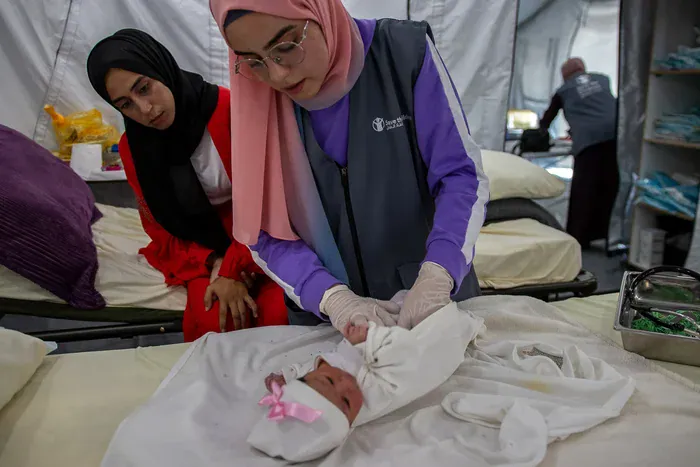 Save the Children midwife Deda* provides a check-up on newborn Lana* while her mother Tima* watches at Save the Children's maternity unit in Gaza.