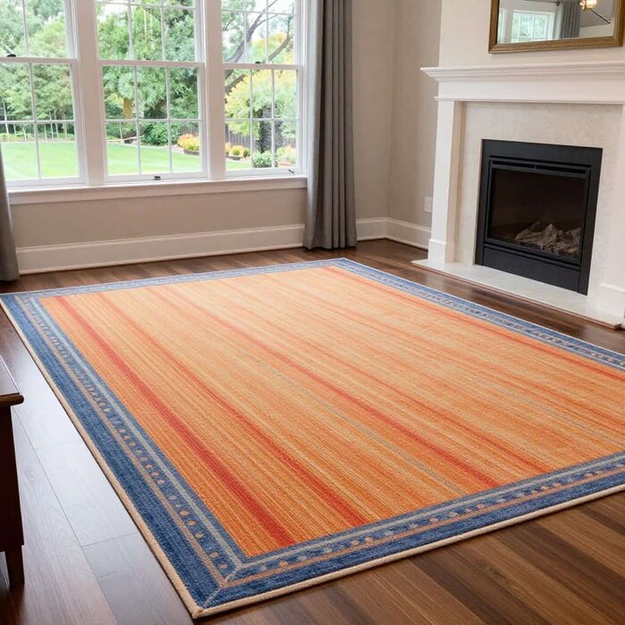 Freshly cleaned orange and blue area rug in a bright living room with large windows.