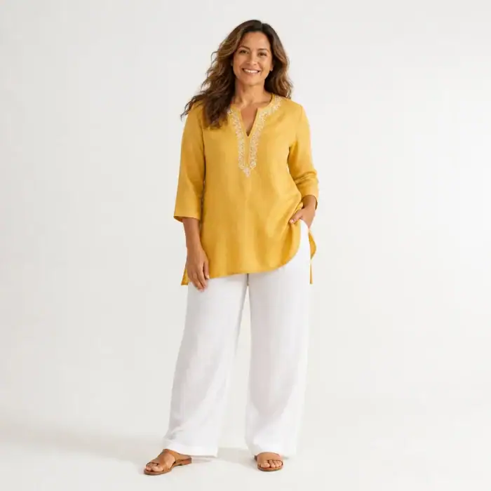 Woman in a mustard linen tunic with an embroidered neckline and white linen trousers