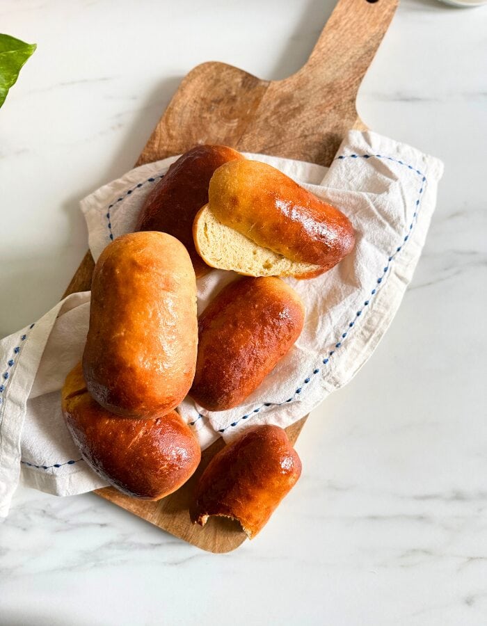 Delicious Vegan Hot Dog Buns 2 from top vegan hot dog buns on a towel on a wooden board, plant behind, on a marble background