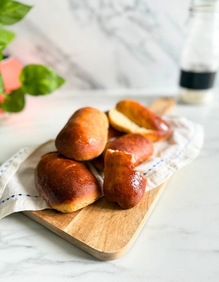 Delicious Vegan Hot Dog Buns 3 vegan hot dog buns on a towel on a wooden board, a bottle of flour and plant behind, on a marble background