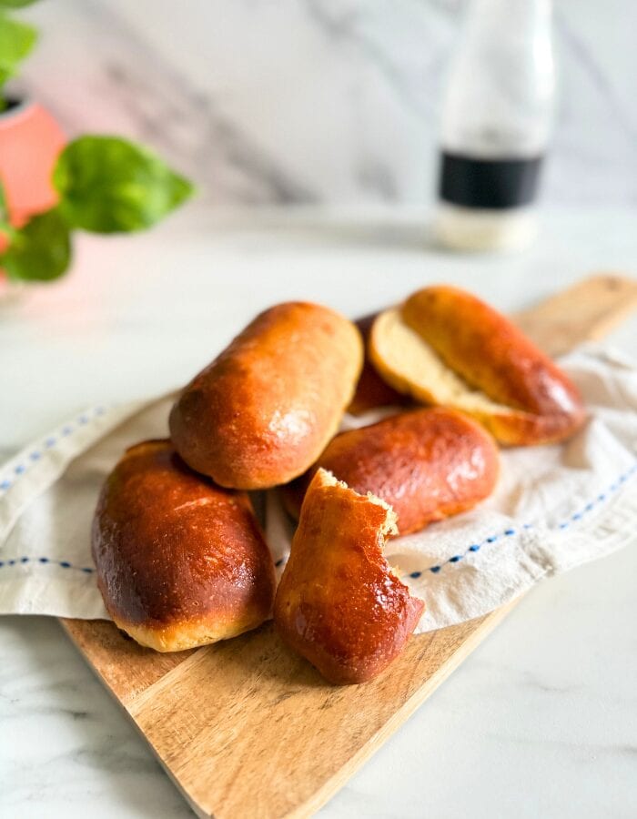 Delicious Vegan Hot Dog Buns 5 close up vegan hot dog buns on a towel on a wooden board, a bottle of flour and plant behind, on a marble background