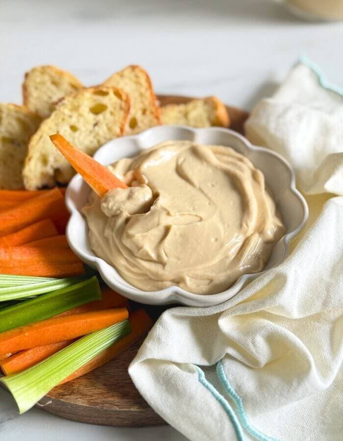 close up bowl of miso mayonnaise, on a wooden board with more veggies cut on the side, slices of bread, towel and a jar of mayo in the back
