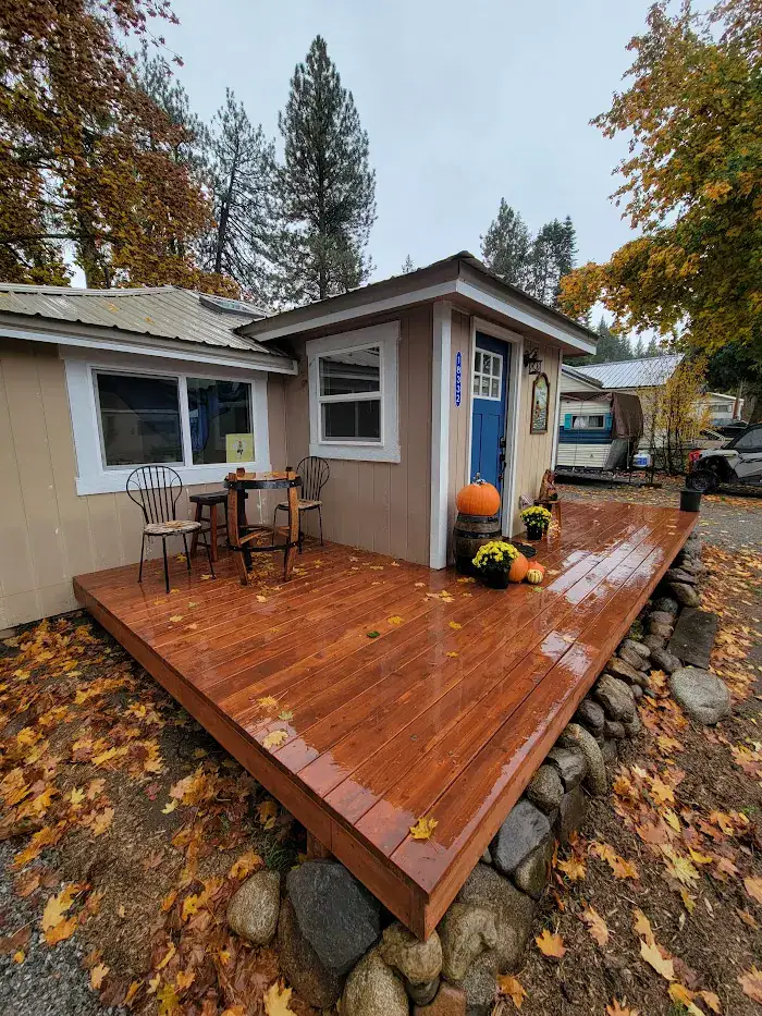 A freshly stained wooden deck built by a Coeur D'Alene handyman, featuring a blue door, autumn decorations, and a stone foundation in a forest setting.