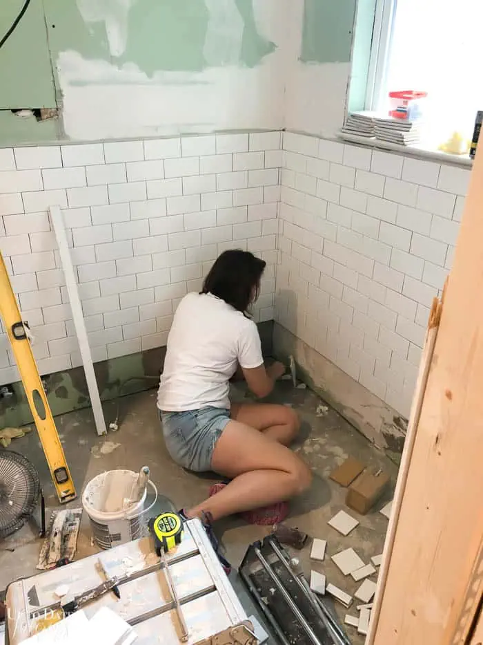 woman install white subway tile in a small bathroom White And Grey Bathroom