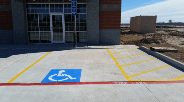 ADA handicap parking stall with blue wheelchair symbol, yellow crosshatch access aisle, yellow stall lines, and red FIRE LANE curb striping at a brick commercial building entrance