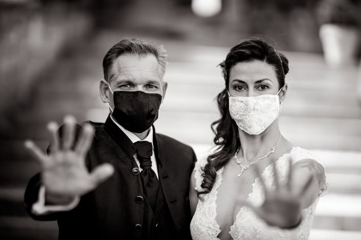 Hochzeit in Corona Zeiten in Schwarz Weiss Braut & Bräutigam tragen einen Mundschutz und halten die Hände abwehrend Richtung Kamera Canon EOS R & RF 85mm