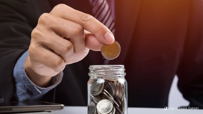 A man inserting a coin into a glass jar, symbolizing saving or investment.