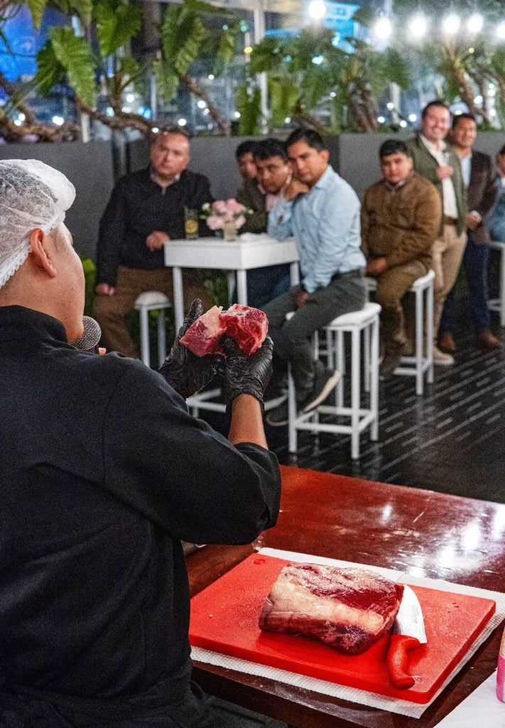 Chef mostrando un corte de carne cruda a un grupo de asistentes durante una clase de parrilla en Miraflores