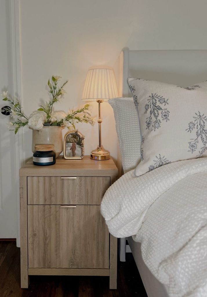 Minimalist bedroom with a bed and nightstand styled with a soft light, framed photo, and candle — elegant bedside table decor ideas for a cozy modern look from By Paige Nicole.