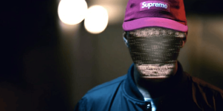 Cinematic music video production shot of British DJ Shy FX wearing a Supreme hat and blue bomber jacket in a dark, atmospheric alley.