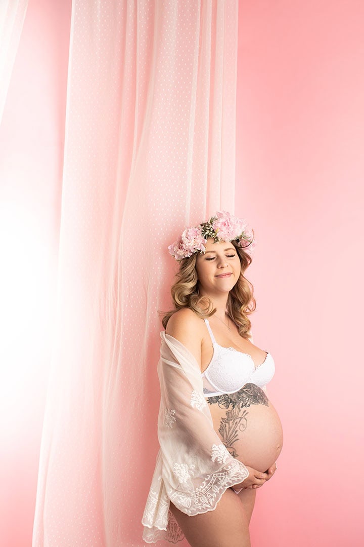 Nydelig gravidfoto av en kvinne med blomsterkrans på hodet, portrett mot rosa bakgrunn, som feirer graviditet uten klær. Perfekt for gravidefotografering og familiegaver.