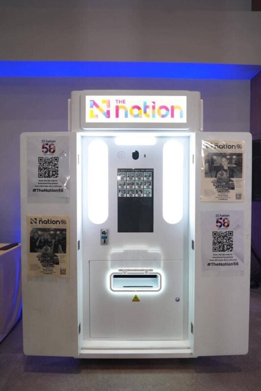 Newspaper photo booth with a branded header sign and sample prints at an indoor corporate event