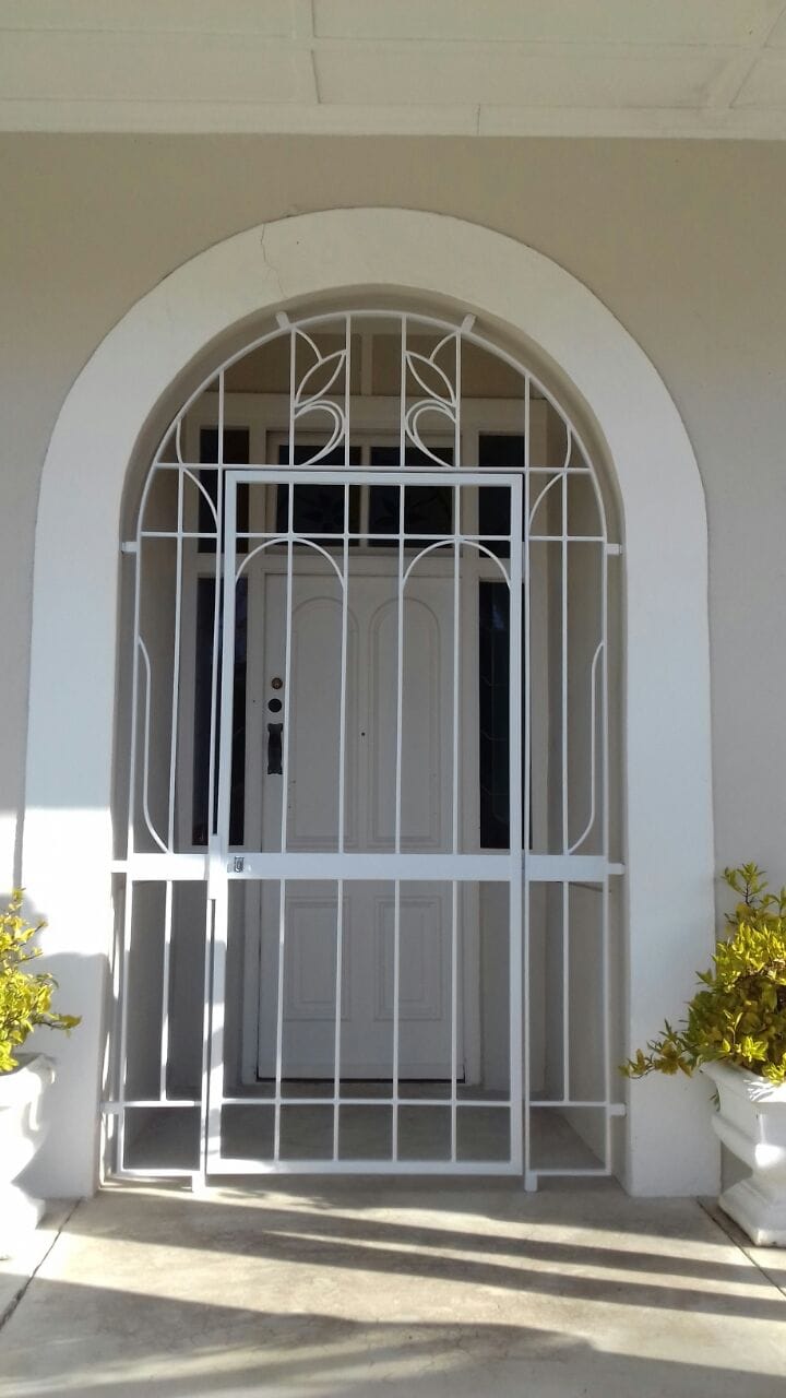 Elegant white arched custom gates featuring leaf-inspired scrollwork framing a recessed front doorway.