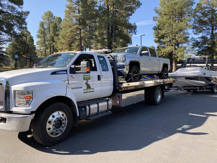 Phoenix flatbed tow truck hauling a truck and boat trailer