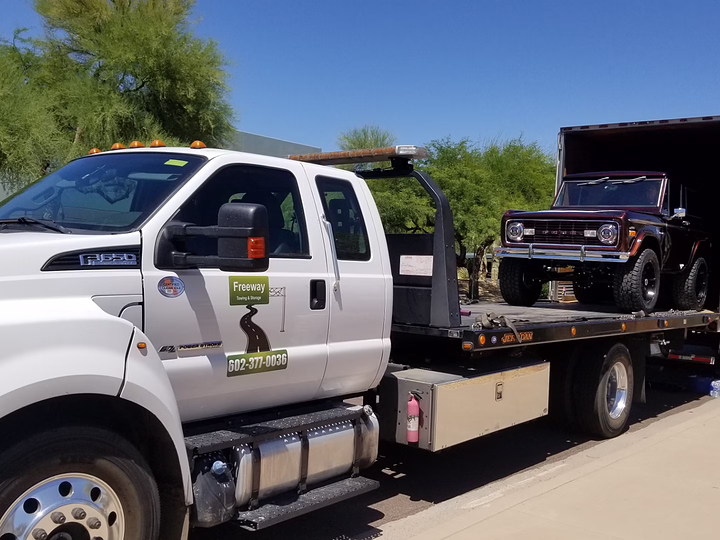 Flatbed tow truck loading a Jeep on a long-haul trailer in Mesa, AZ