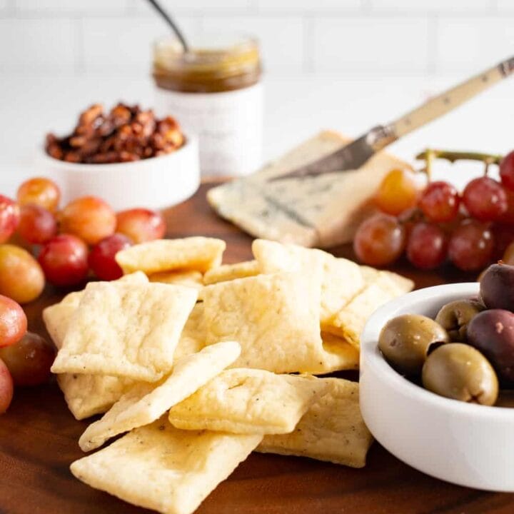 snack board with pecorino crackers, blue cheese, grapes, olives, candied walnuts, and pepper jelly