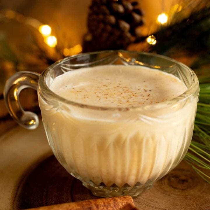 glass of egg nog surrounded by holiday greenery and lights