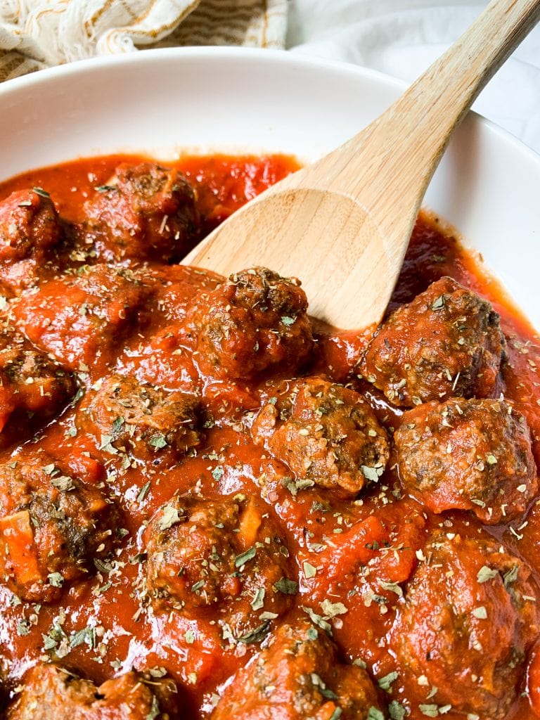 air fryer meatballs in sauce with a wooden spatula in a white bowl