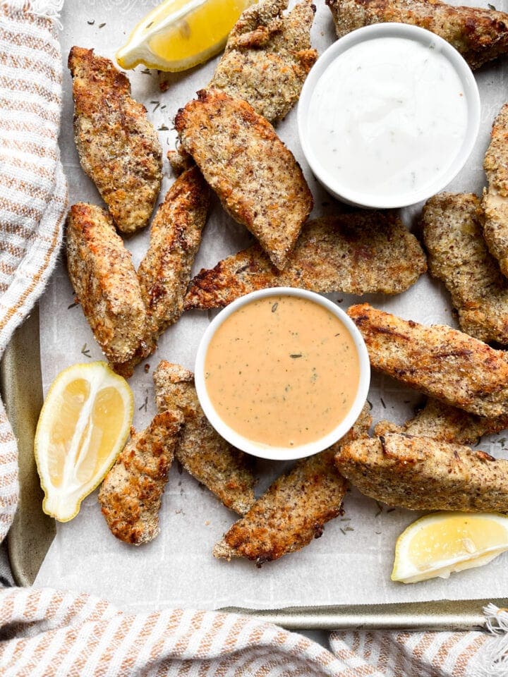 keto chicken strips on a cookie sheet after baking with lemon wedges