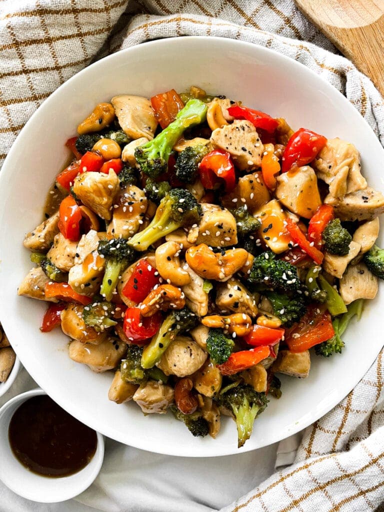 Bowl of Thai Cashew Chicken topped with sesame seeds for garnish next to a bowl of soy sauce