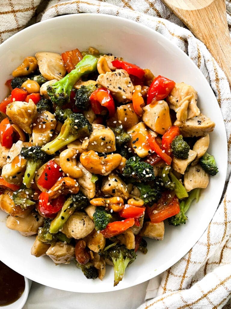 top view of thai chicken with cashews in a white bowl next to a wooden spoon