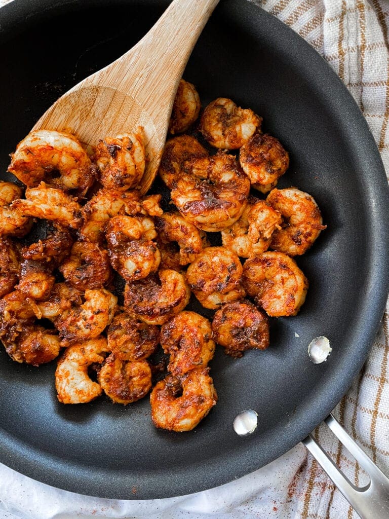 blackened shrimp in skillet on stove top with wooden spoon