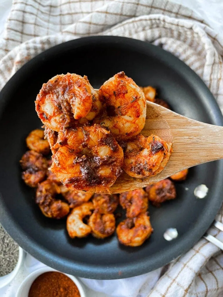 four blackened shrimp on a wooden spoon over a skillet