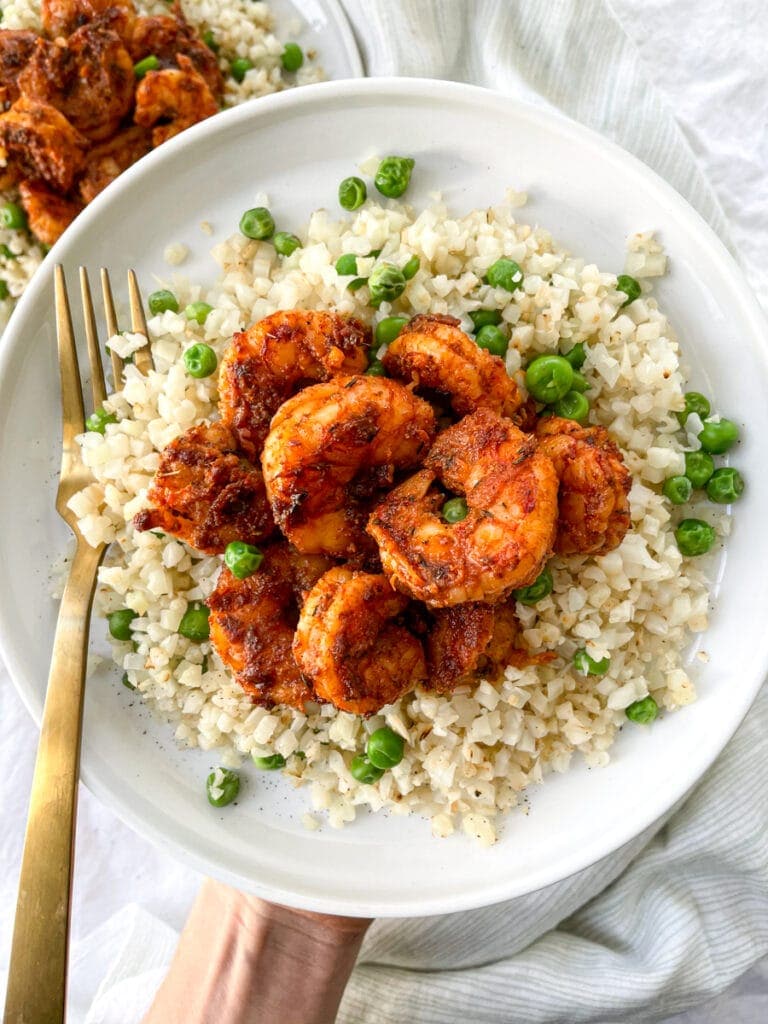 blackened shrimp over cauliflower rice on white plate with gold fork