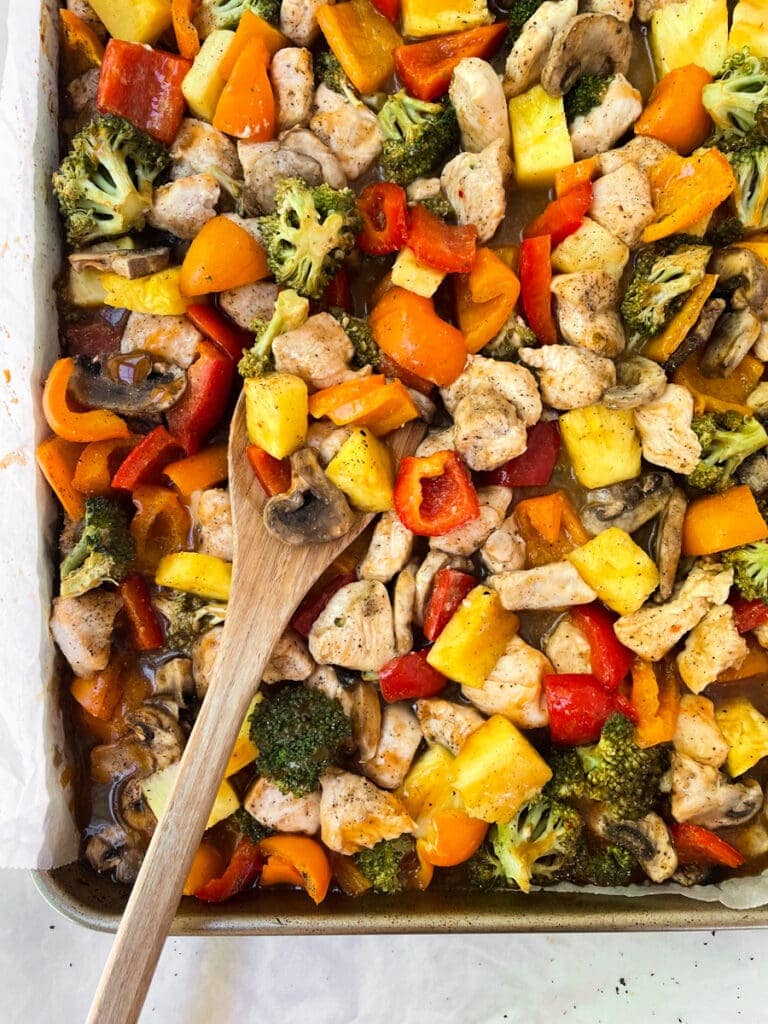 hawaiian sheet pan chicken and veggies with a wooden spoon on the pan