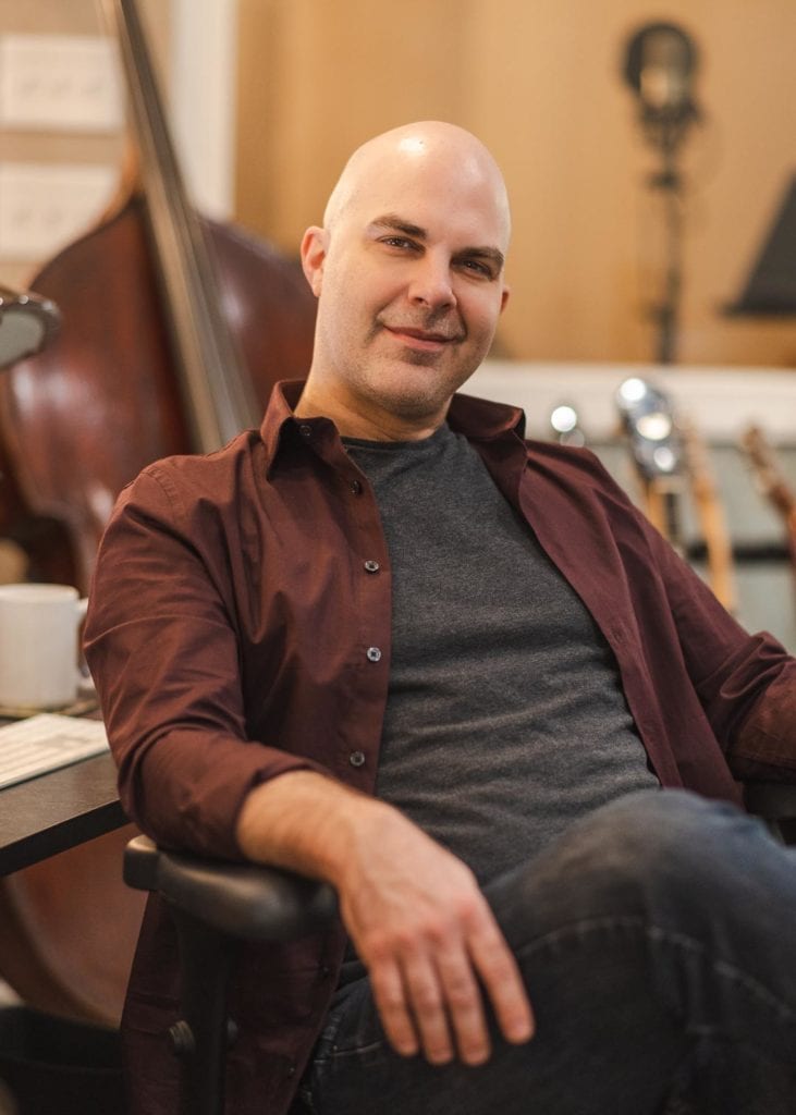 Music producer Will Robertson sitting in a chair at his desk and smiling