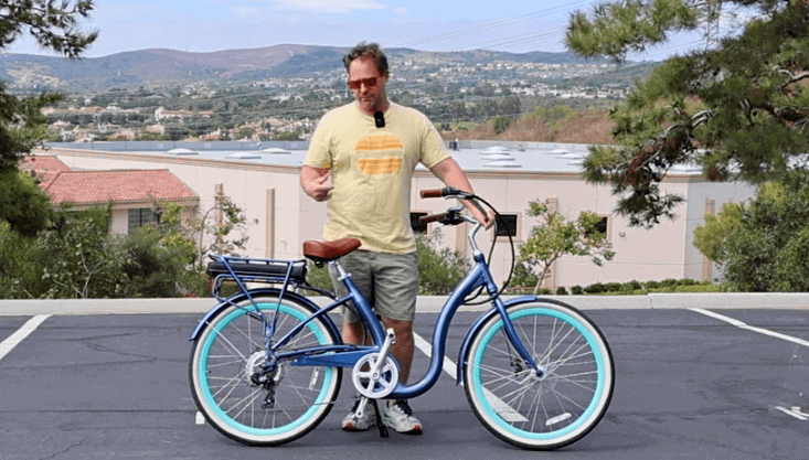 Man standing beside a blue beach cruiser electric bike in a parking lot