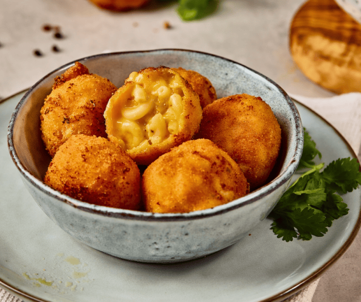 A crispy golden brown Mac and Cheese Bite broken open to show the gooey melted cheese and elbow macaroni inside.
