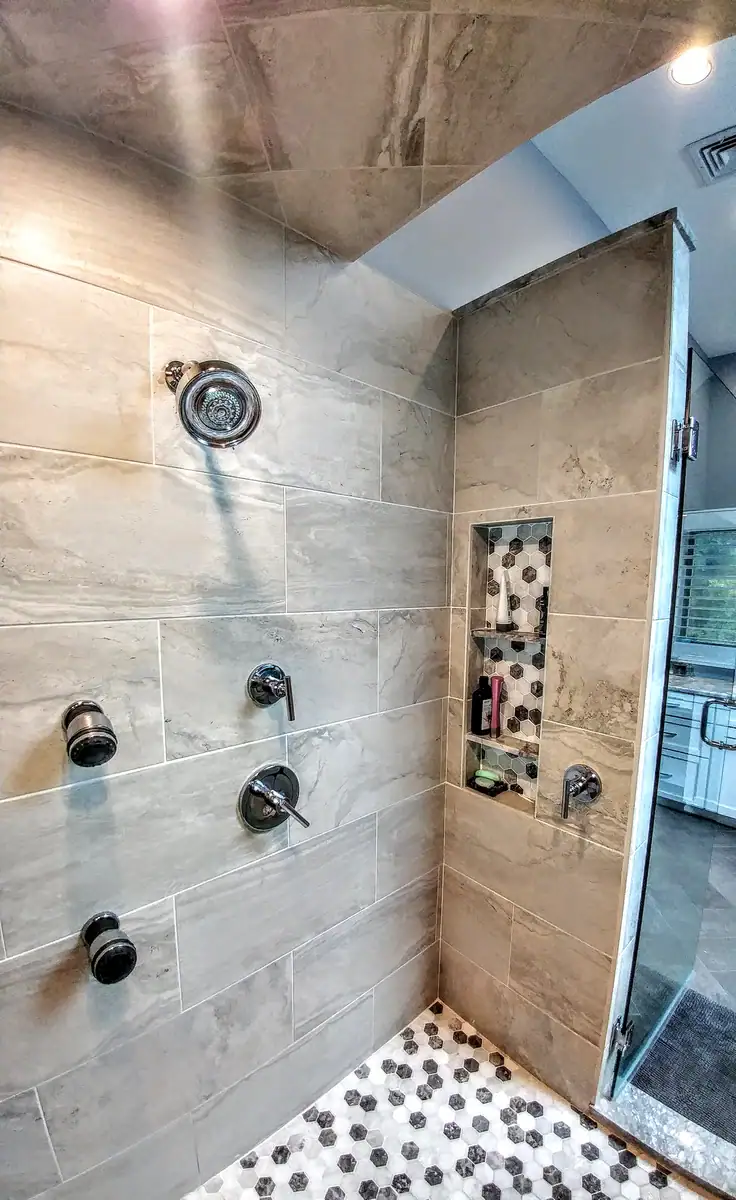 Tiled shower enclosure showing a glass door, custom storage niche, and light gray stone-look wall tiles.