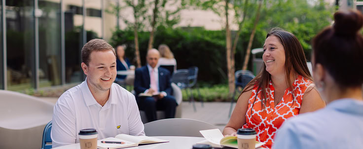 Three coworkers enjoy a working coffee in the outdoor patio of a luxury Raleigh office building