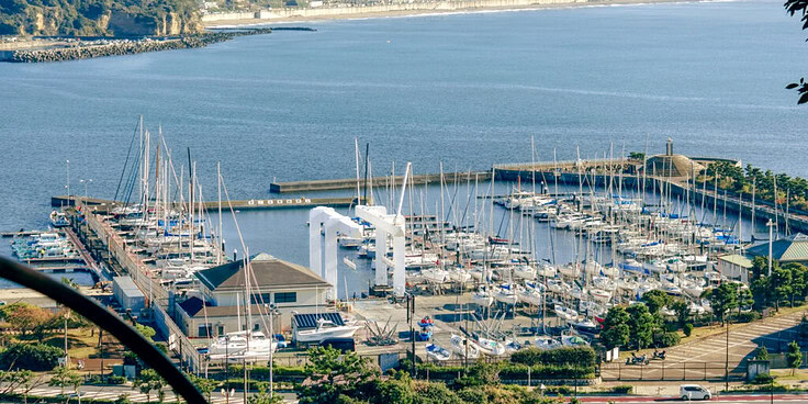 A scenic view from Enoshima Island showcasing a marina with sailboats, a calm ocean, and the coastal town in the background under a clear sky.