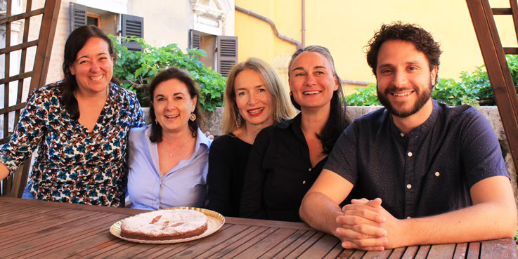 Eine fröhliche Gruppe von Menschen sitzt an einem Holztisch im Freien mit einem traditionellen italienischen Kuchen.