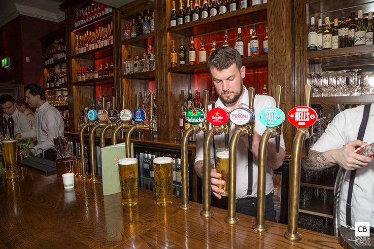 The refurbed bar at the The Park Teddington is made with dark wood panels, copper pipes and dark red accents. 