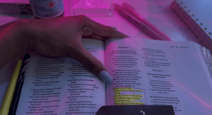Woman’s hand holding an open Bible with Psalm 56:3–4 highlighted under pink lighting