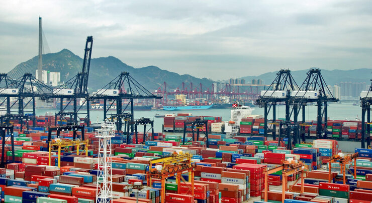 Cargo containers and U.S. Customs officers at a busy port, illustrating the impact of tariffs and trade policy on imported goods.