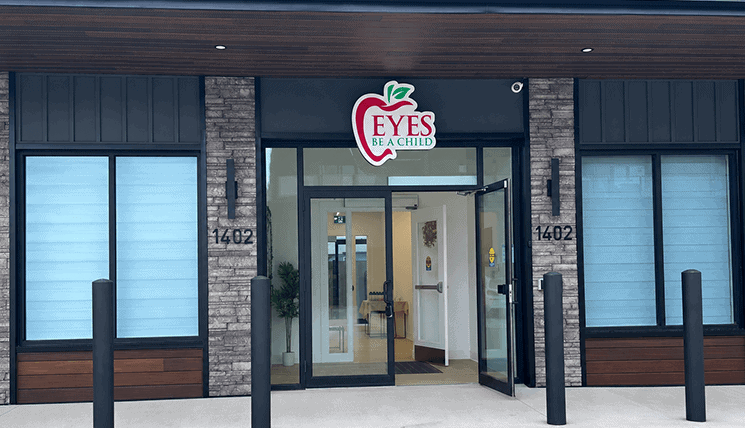 eyes-childcare-tillsonburg Front entrance of an 'Eyes Be a Child' clinic, glass doors open, with a brick and wood façade and the address 1402 on both sides.