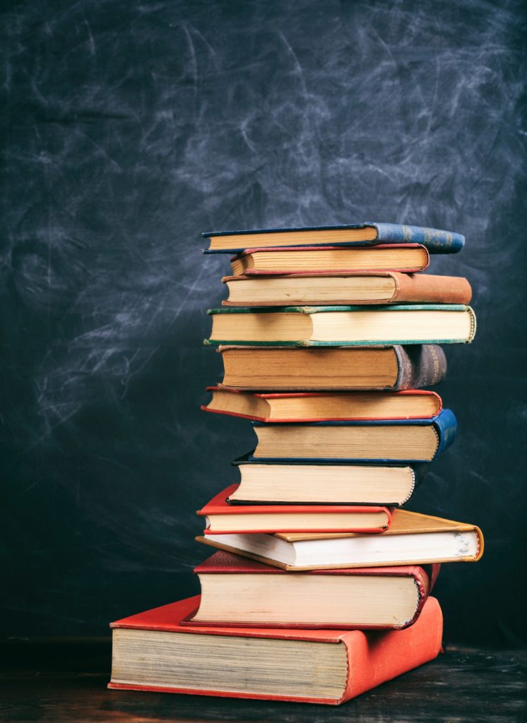 A stack of books sits on a table against a dark blue backdrop