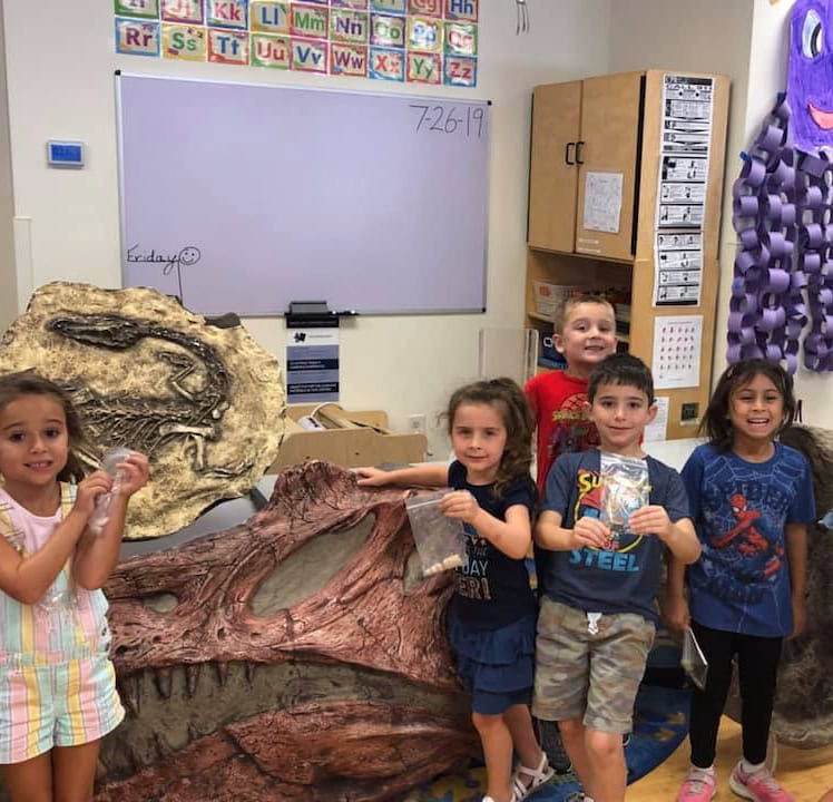 campers standing next to a spinosaurus skull and a coelophysis skeleton in the background
