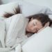A woman dressed in white sleeping in a bed with white bedding showcasing the best comforter for hot sleepers.