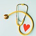 medical stethoscope with red paper heart on white surface